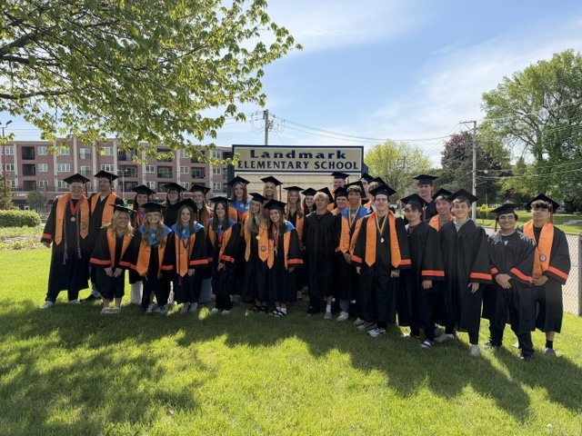 Students in caps and gowns standing in front of Landmark sign 