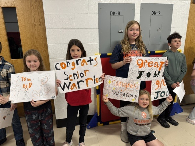 Elementary students holding sings that say "You did it. "Congrats senior Warriors" "Great Job"