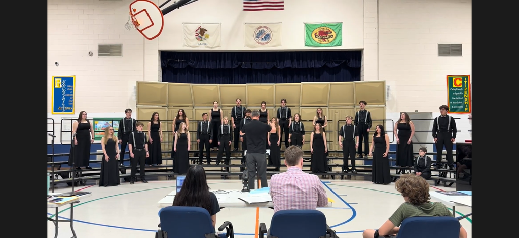 Choir director directing choir students that are all dressed in black in a gym