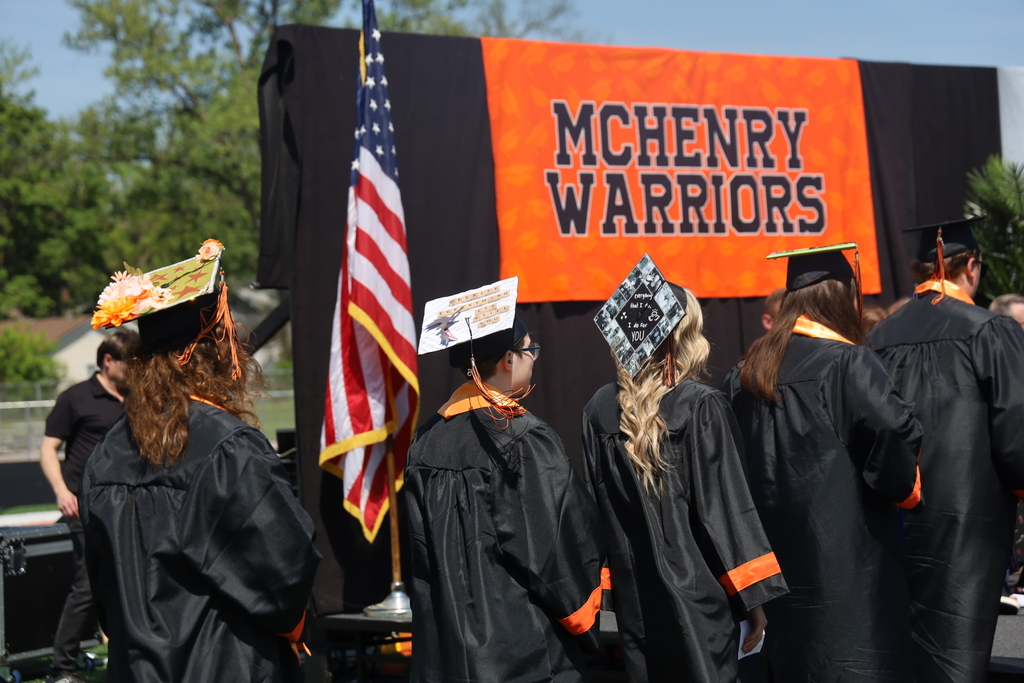 Decorated grad caps by American flag and McHenry Warriors Sign 