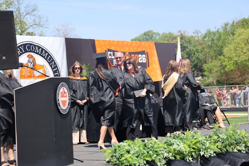 Students walking on the stage at graduation School board president holding diploma and shaking hand