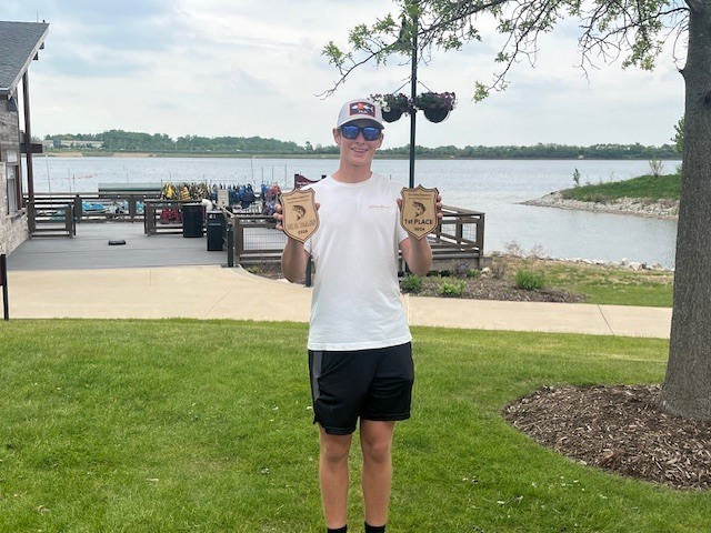 Student holding two trophies by the lake 