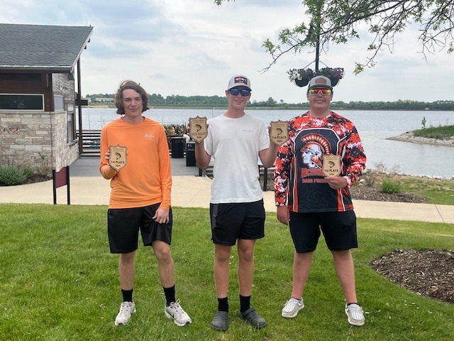 Three students holding four trophies by the lake 