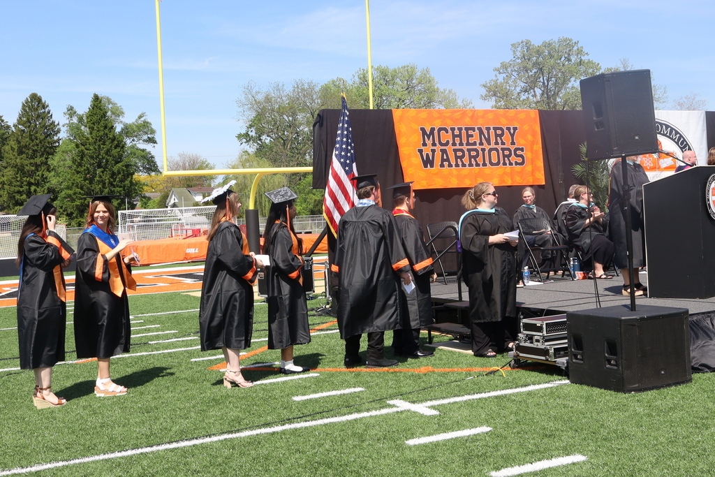 Graduates standing by stage on the football field