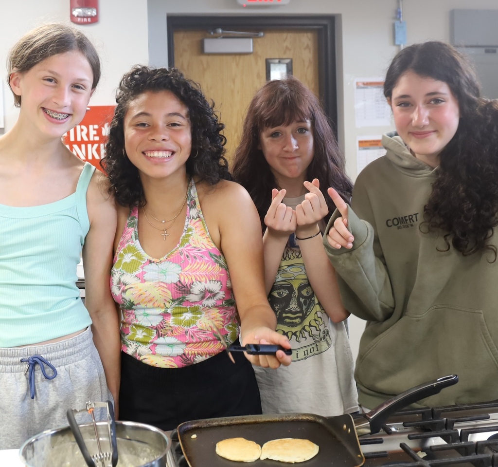Four students posing in front of pancakes on a pan