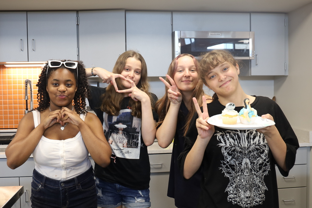Four students doing heart signs and peace signs and one holding two decorated cupcakes
