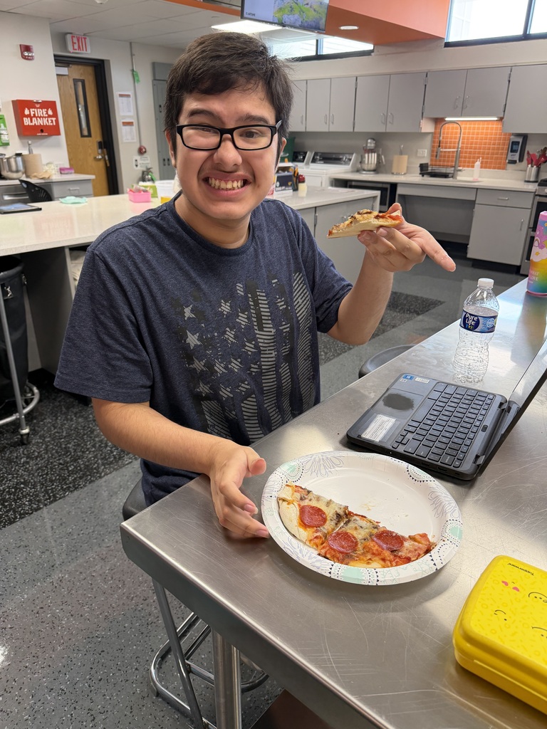 Student smiling holding a slice of pizza
