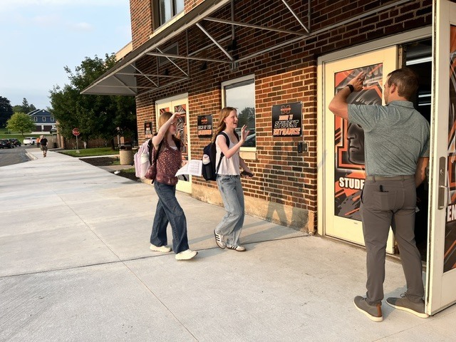 Two students waving at the Freshman Campus principal walking into Freshman Campus