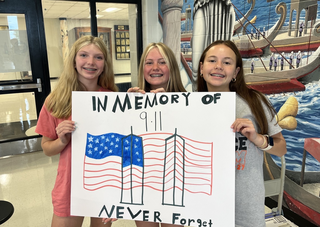 Studnets holding up a poster that says 9/11 in memory of with flag and twin towers never forget