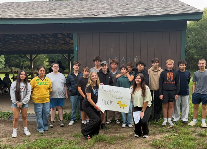 Student AIM group posing at camp and holding a sign