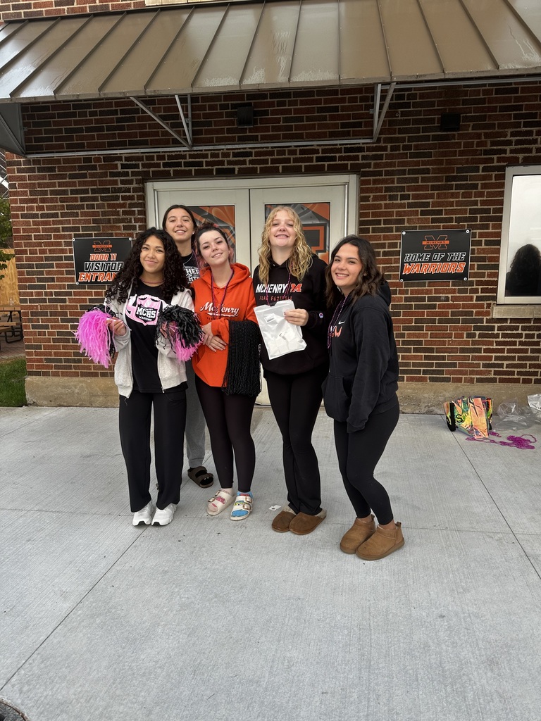 Four students standing in front of Freshman Campus one holding pom poms