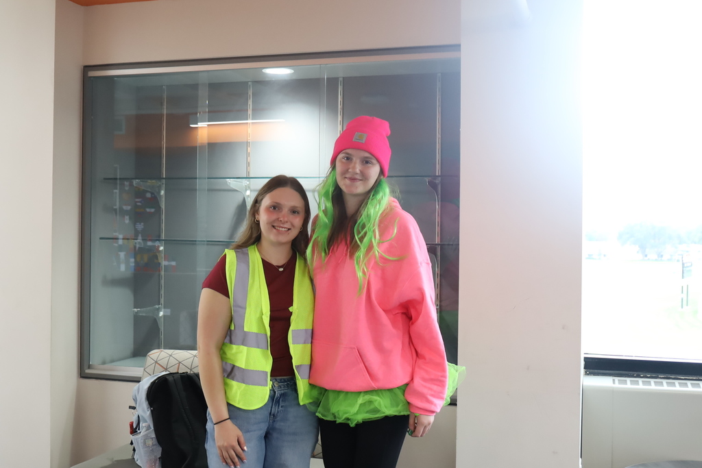 Two students in neon construction vest and one in green wig and tutu, neon pink shirt and hat
