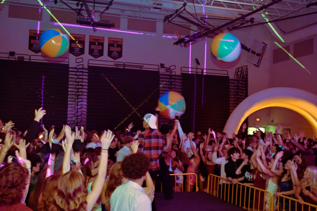 Gym with students throwing hands up and beach balls in the air