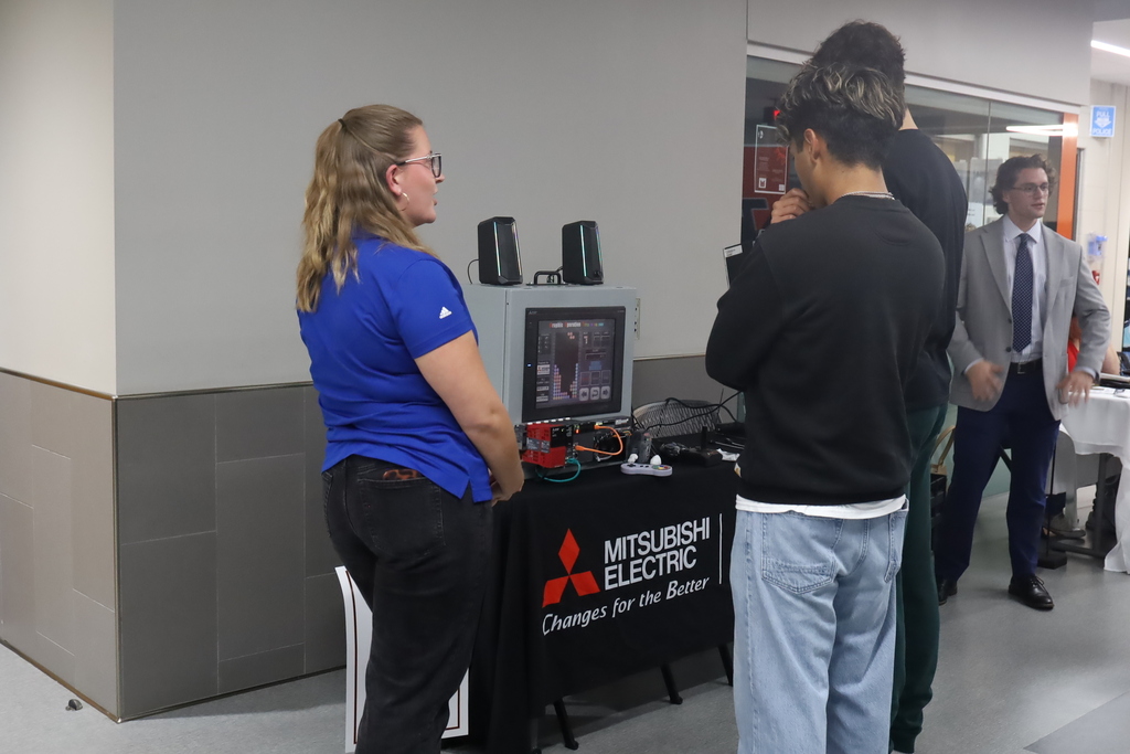 Students talking at the Mitsubishi Electric booth with a machine in front of them