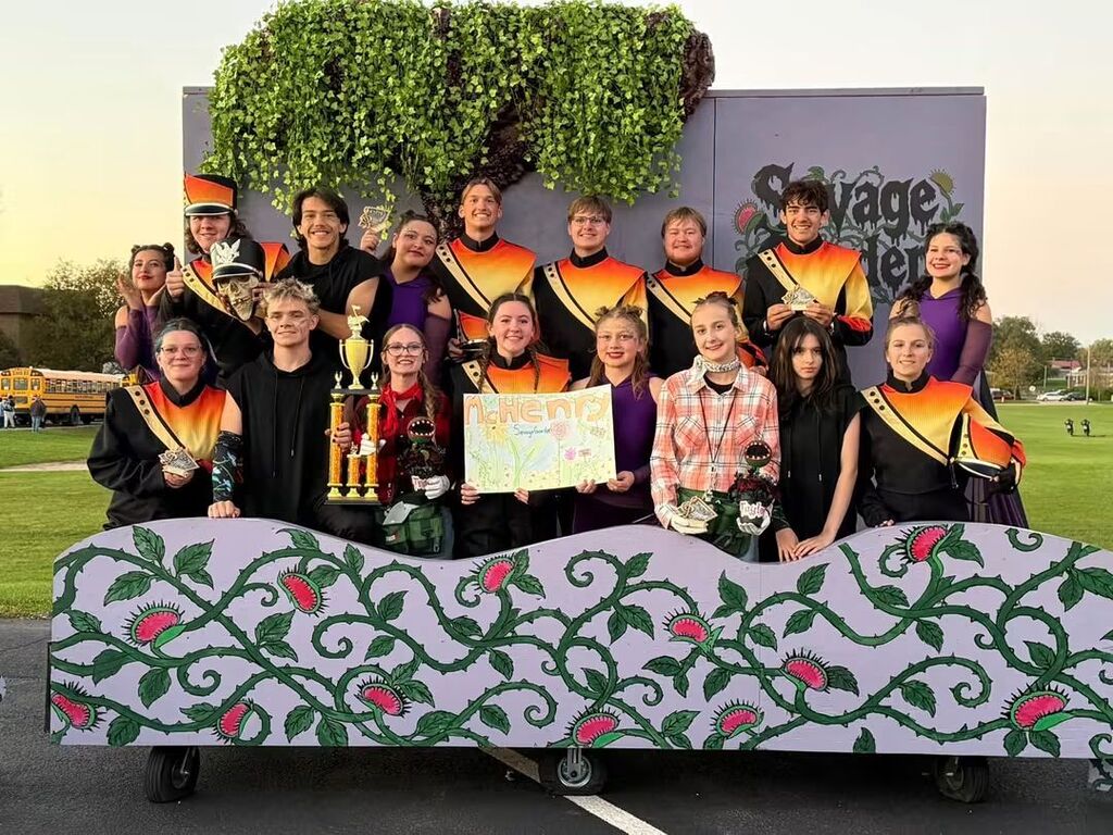 Marching band with McHenry standing in front of Savage Garden decor and holding trophy