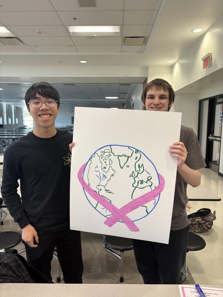 Two students holding a sign with the earth with a pink ribbon wrapped around it. 