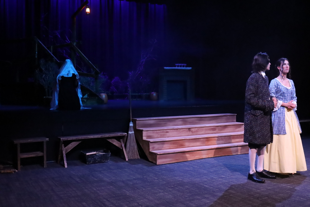 Two characters standing by a creepy stage with a ghost