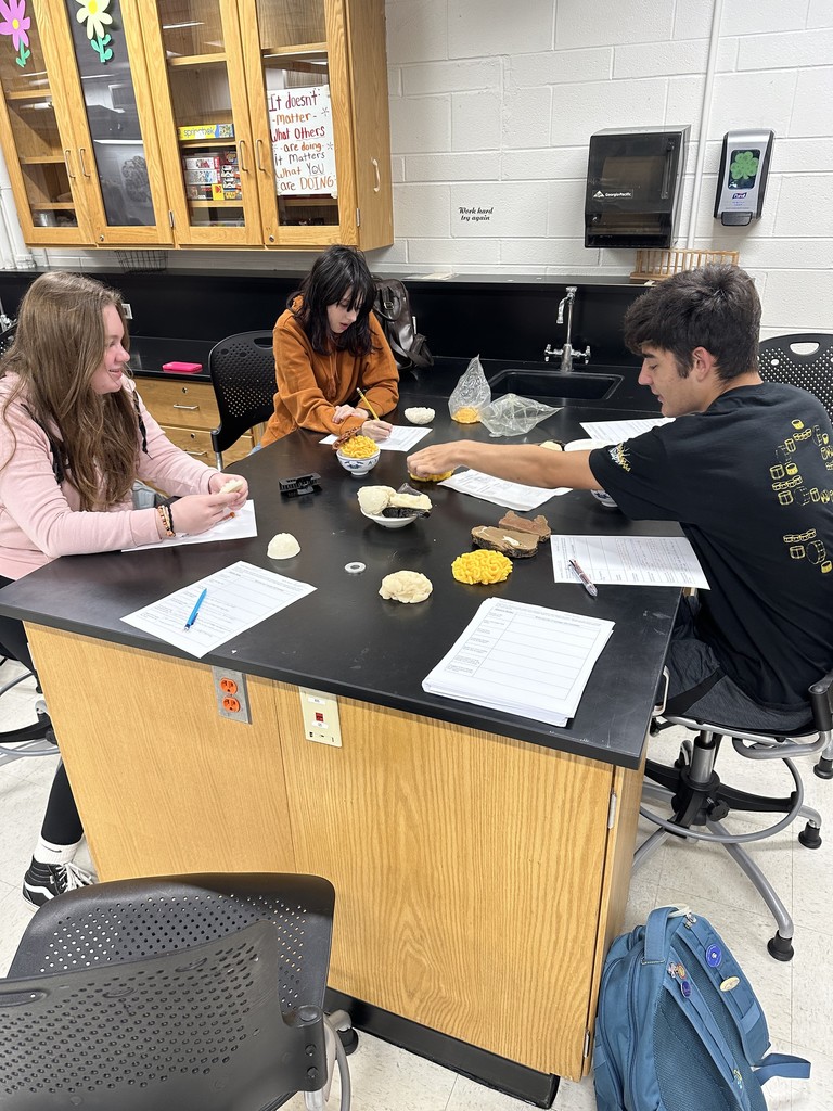 Students looking at fake food for measurements at a lab table with worksheets in front of them
