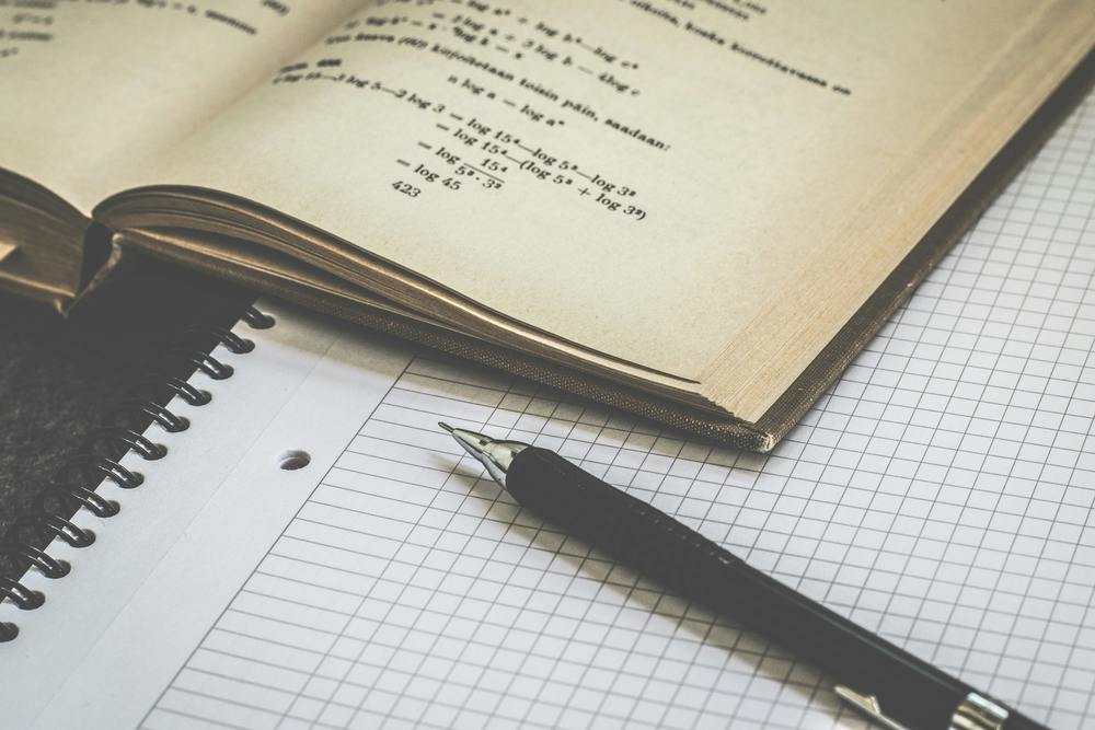 Math textbook resting on top of a gird paper spiral notebook.