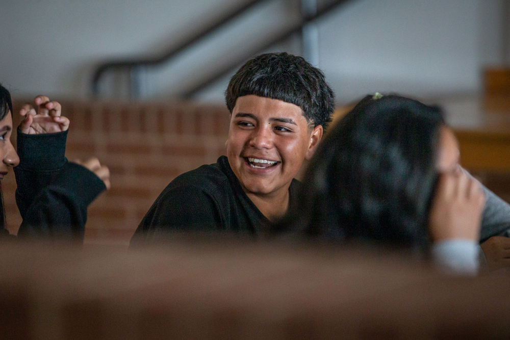 male student at table looking at a friend and lauging as they talk
