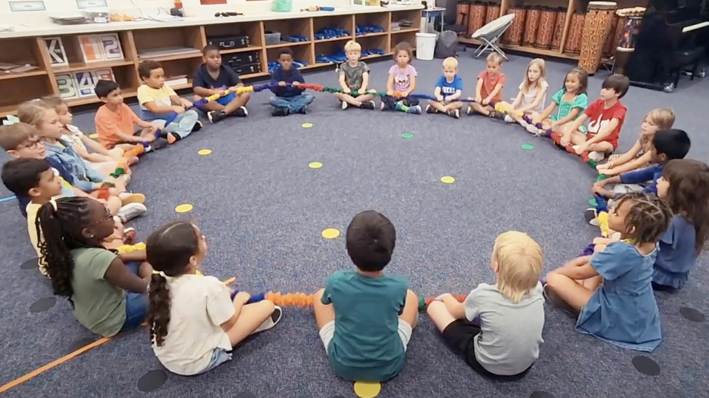 children sitting cross legged in a circle holding a large cloth hoop