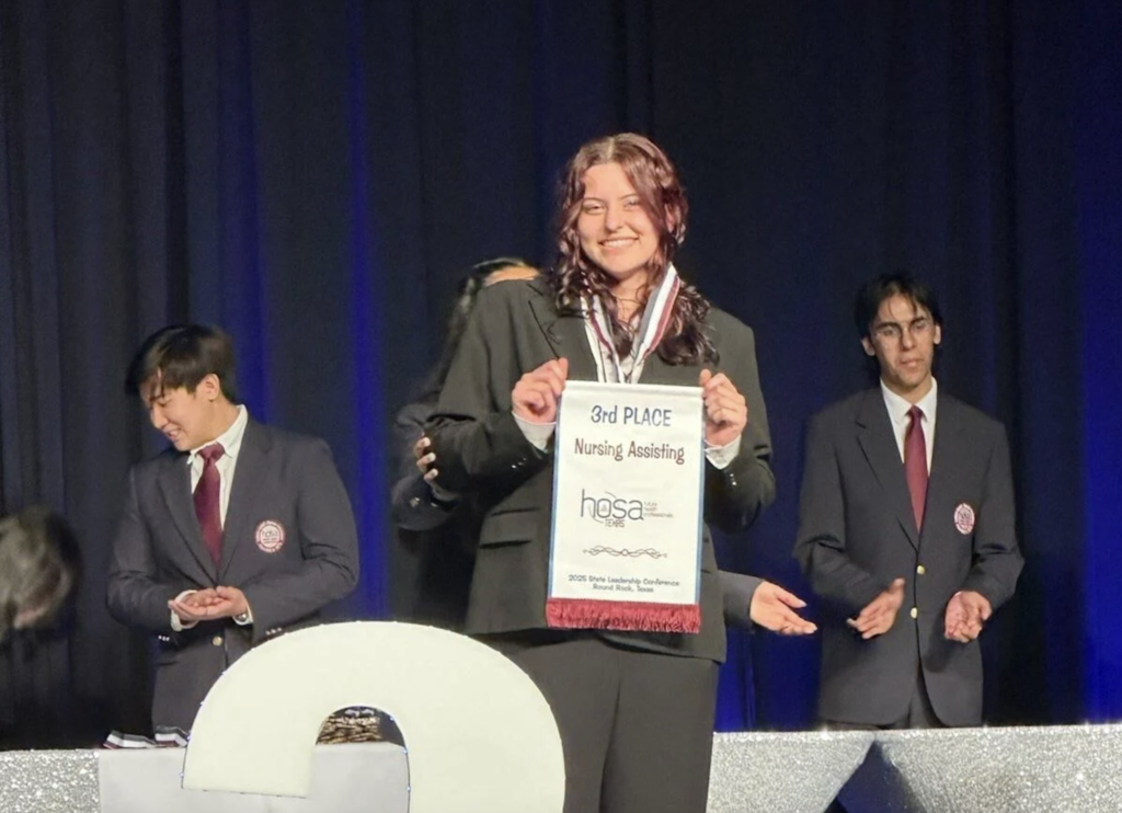 female competitor on stage smiling and holding up 3rd Place banner