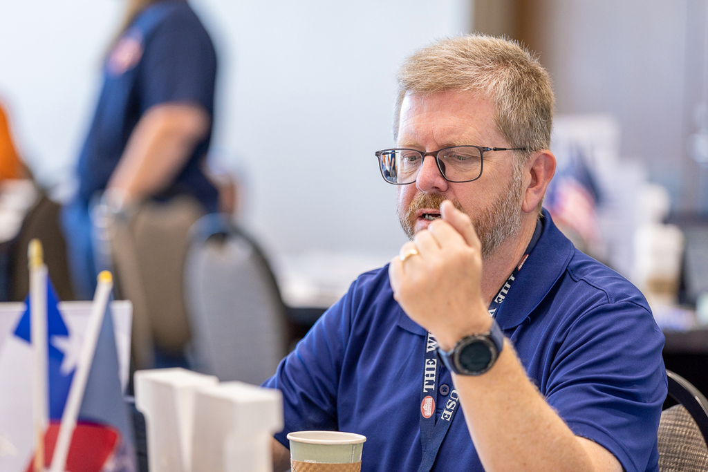 male teacher at table talking with a colleague while looking at information on computer