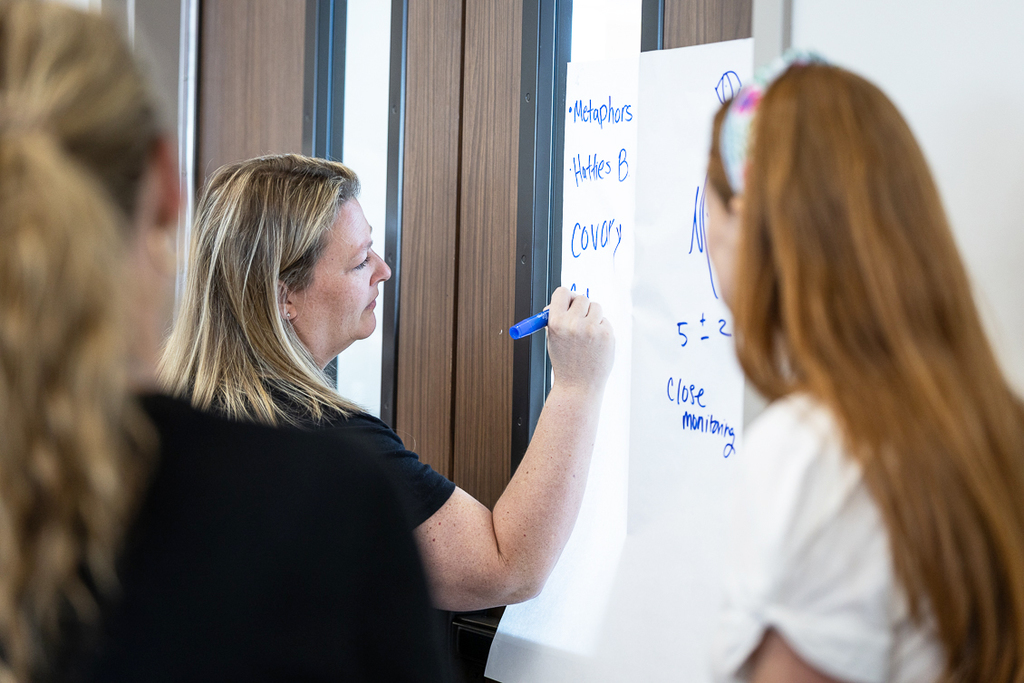 female teachers writing responses on large sheet of paper during workshop