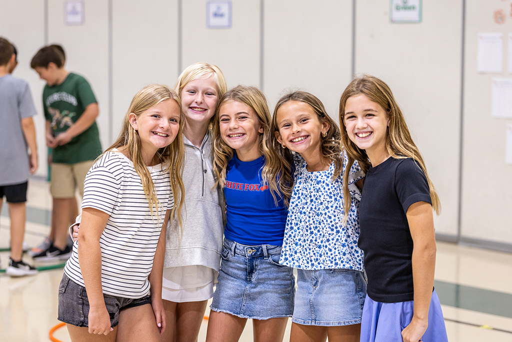 group of five girls with arms around shoulders smiling for the camera