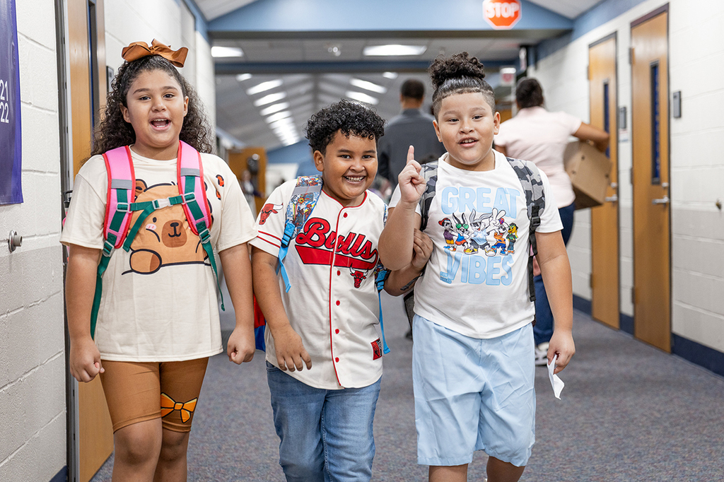 one girl and two boys walking down the hall side by side with one of the boys talking and gesturing