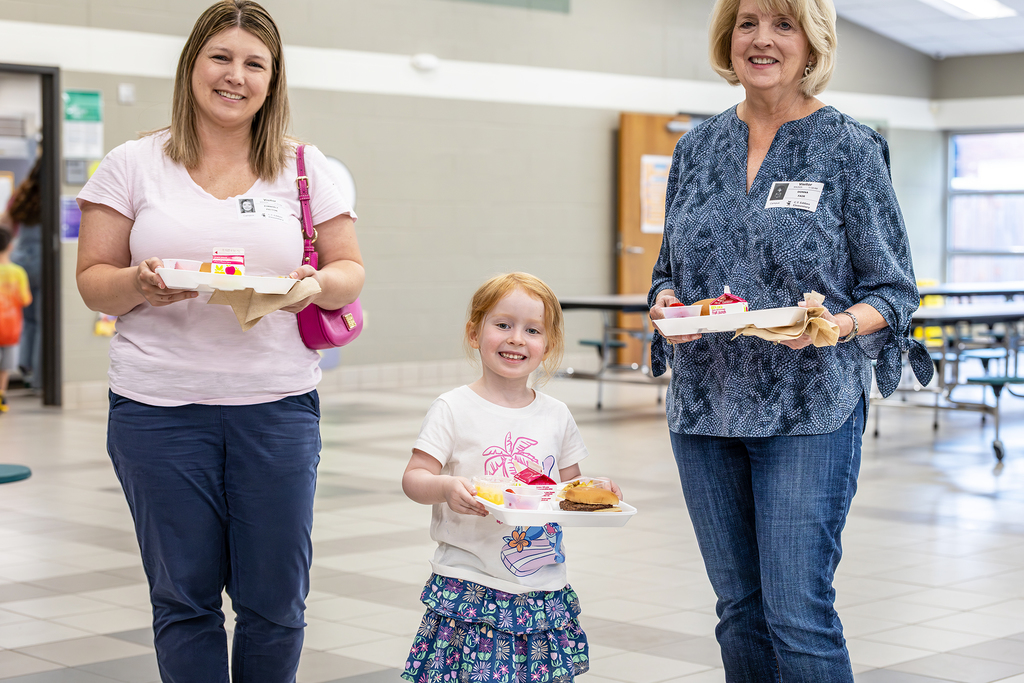 small girl and two adult women holding their lunch trays and posing for pic