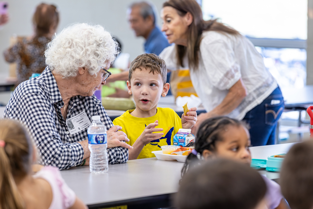 grandson seated at table explaining something to grandmother as she listens attentively