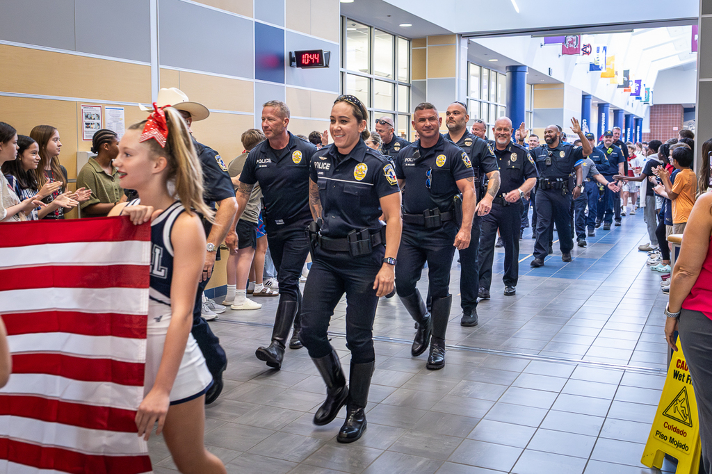 long line of police officers and firefighters walking through the Cockrill main hallway as students cheer