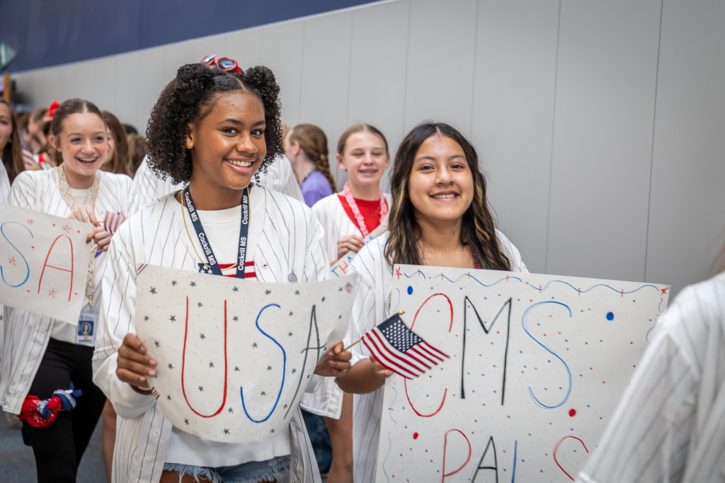girls holding USA and CMS PALS signs among a group walking down the hall at Cockrill Middle School