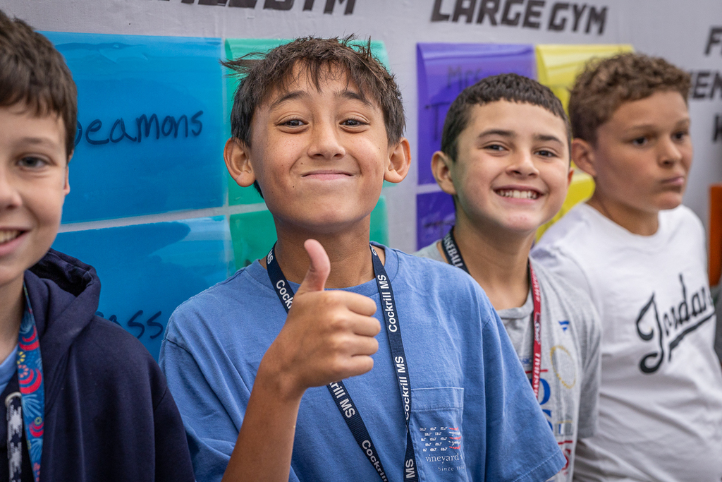 three smiling boys in the hallway with one boy giving a thumbs up