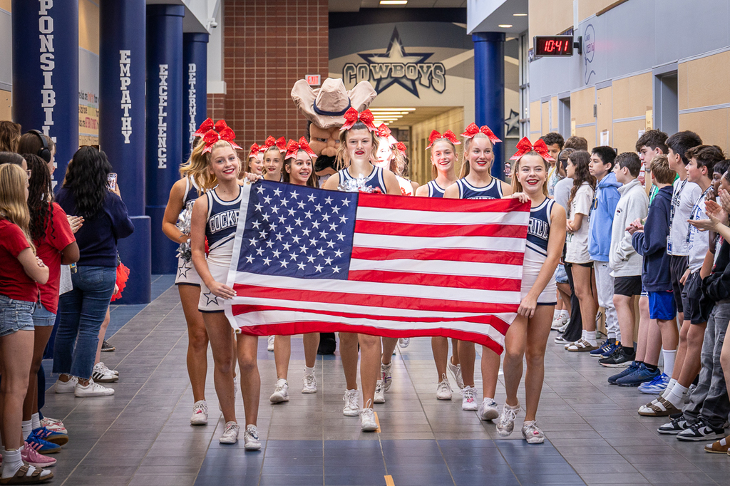 cheerleaders lead the parade holding an American flag