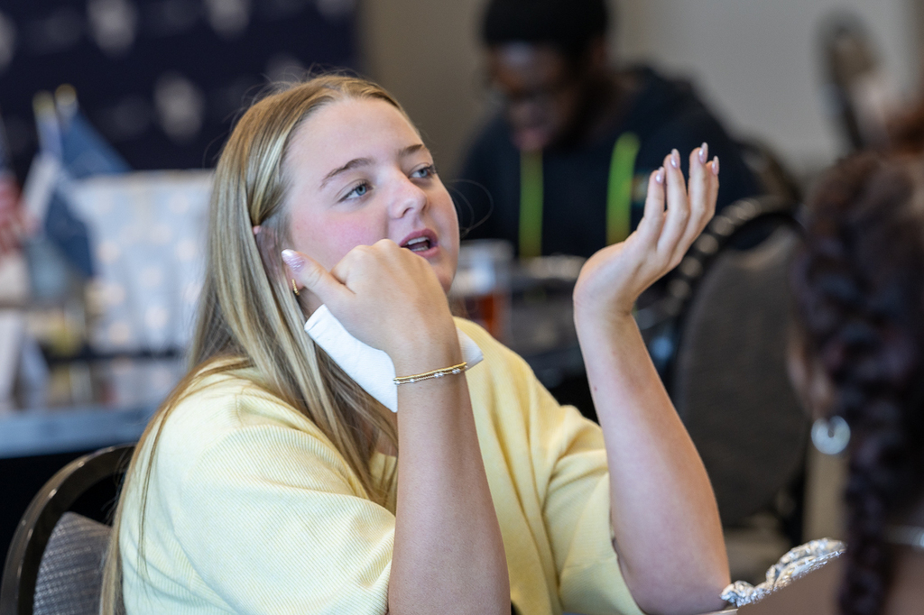 female student gesturing and speaking at her table