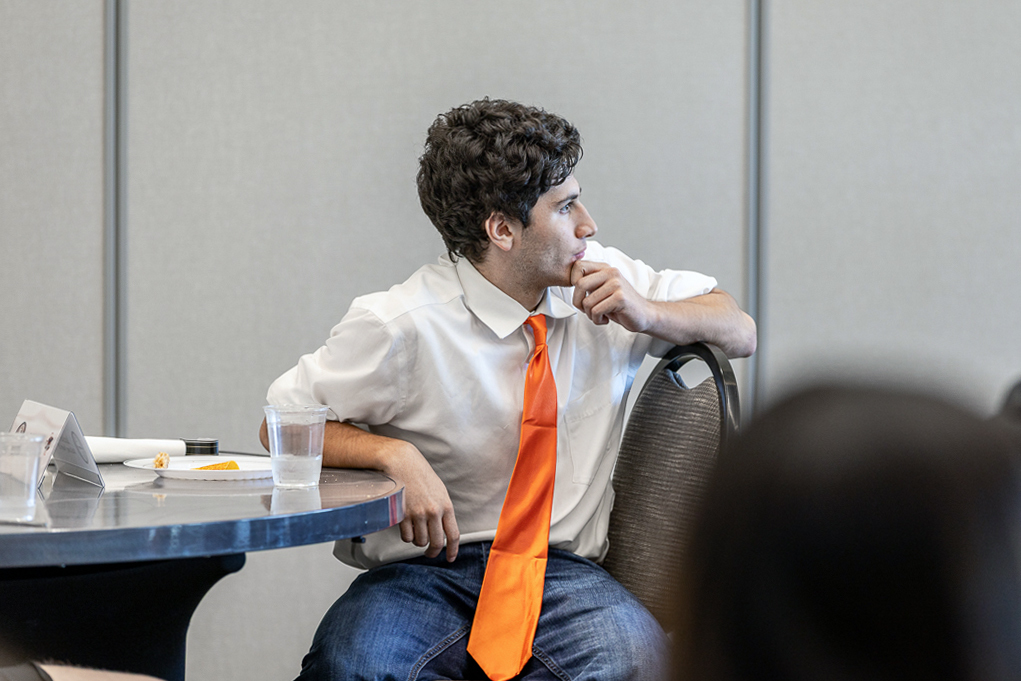 male student seated and looking over toward another table as he listens
