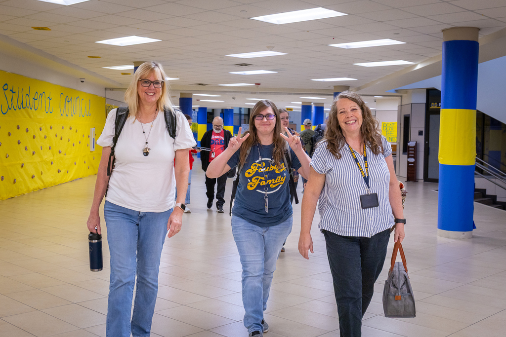 three female teachers walking in hallway and one is making a peace sign gesture