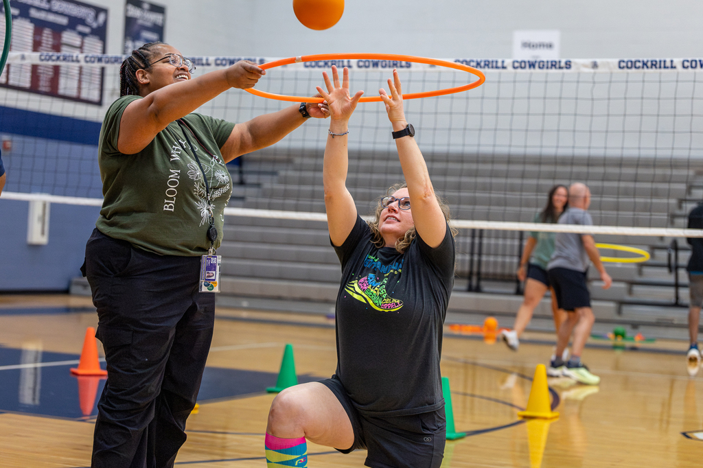 PE teacher reaching up through hoop on one knee to catch a ball