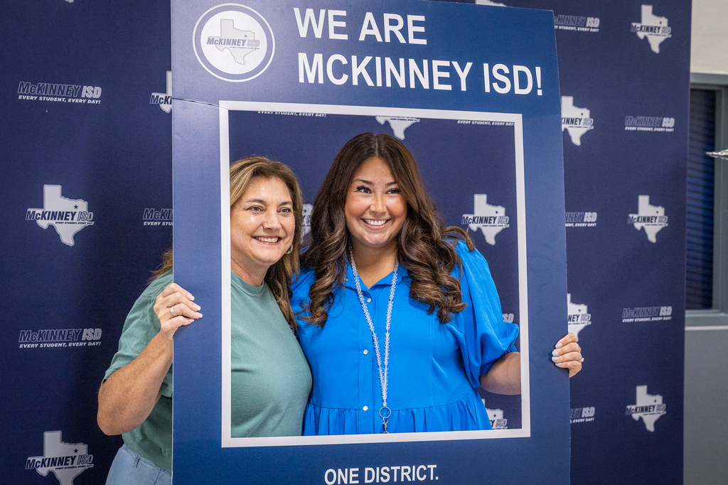 two female teachers holding we are mckinney isd frame for photo against logo backdrop