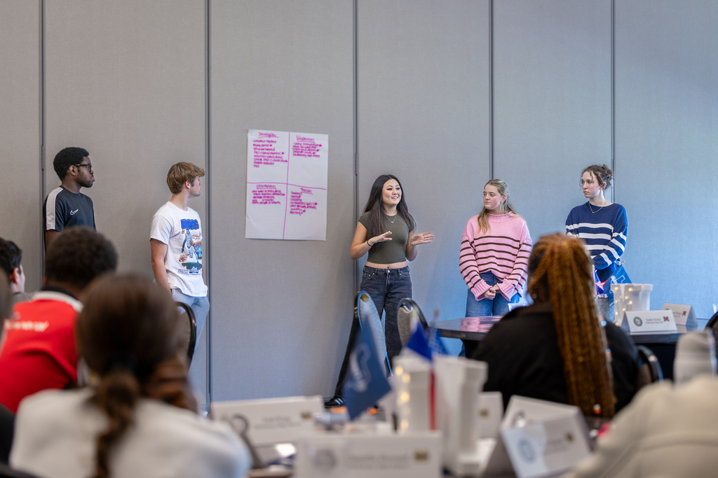 group of male and female students standing by poster board with one girl discussing the information on it