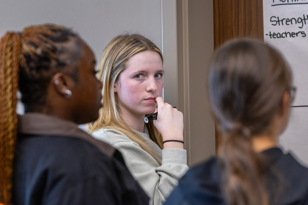 female student with marker in hand looking at the camera as she works in a group