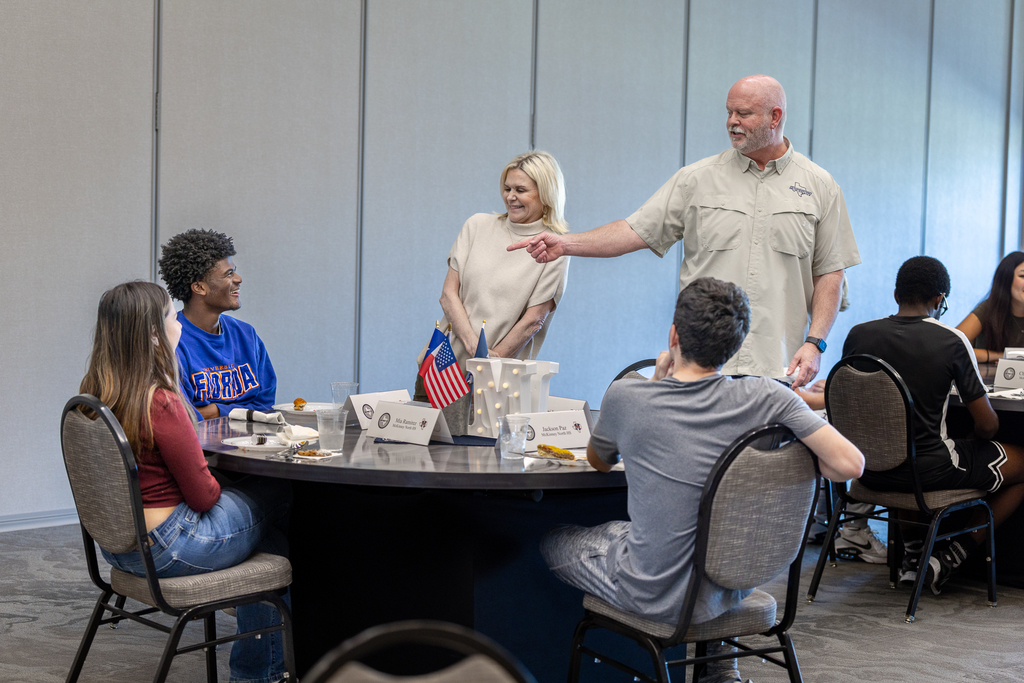 Shawn Pratt and Melanie Raleeh laughing with a student seated a table