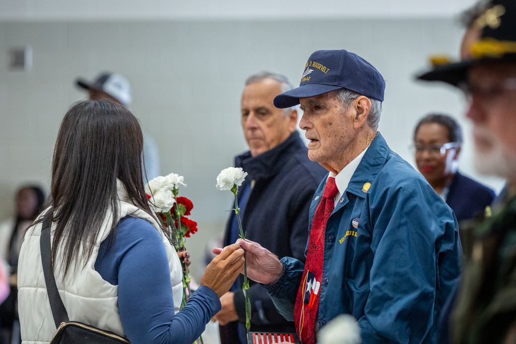 Veteran wearing Navy cap and jacket for the USS Roosevelt accepting a flower from a staff member