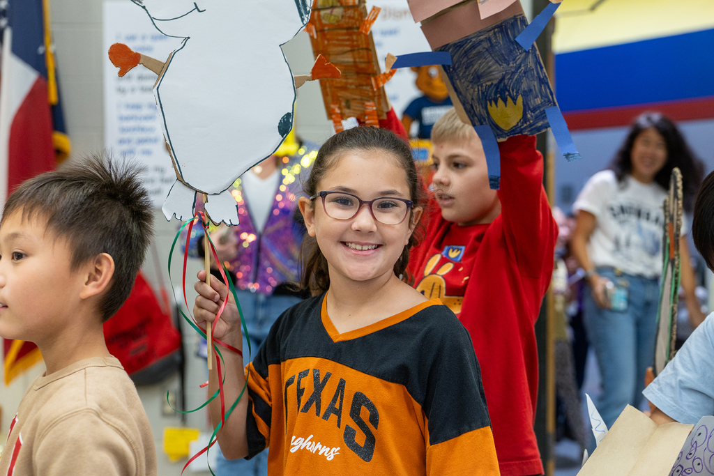 girl smiling at camera in line as she holds up her parade decoration