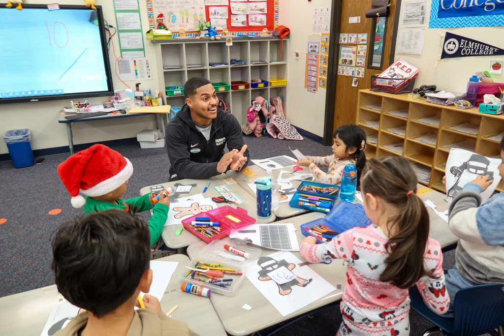 Harding player smiling and clapping as he does art at a table with young students