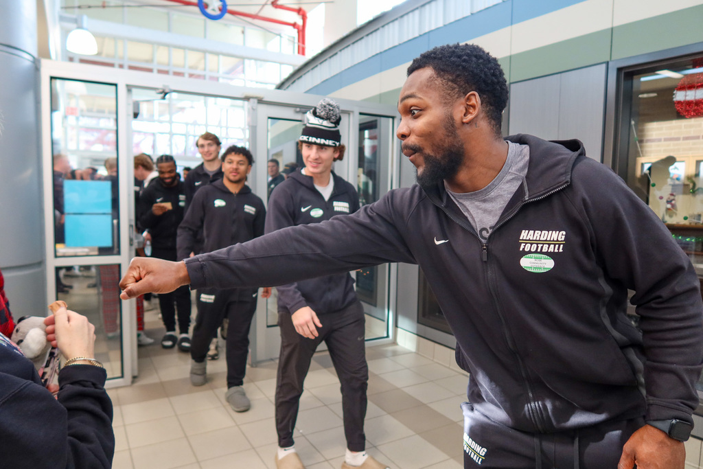 A Harding player reaches out to fist bump a student as the group enters the school