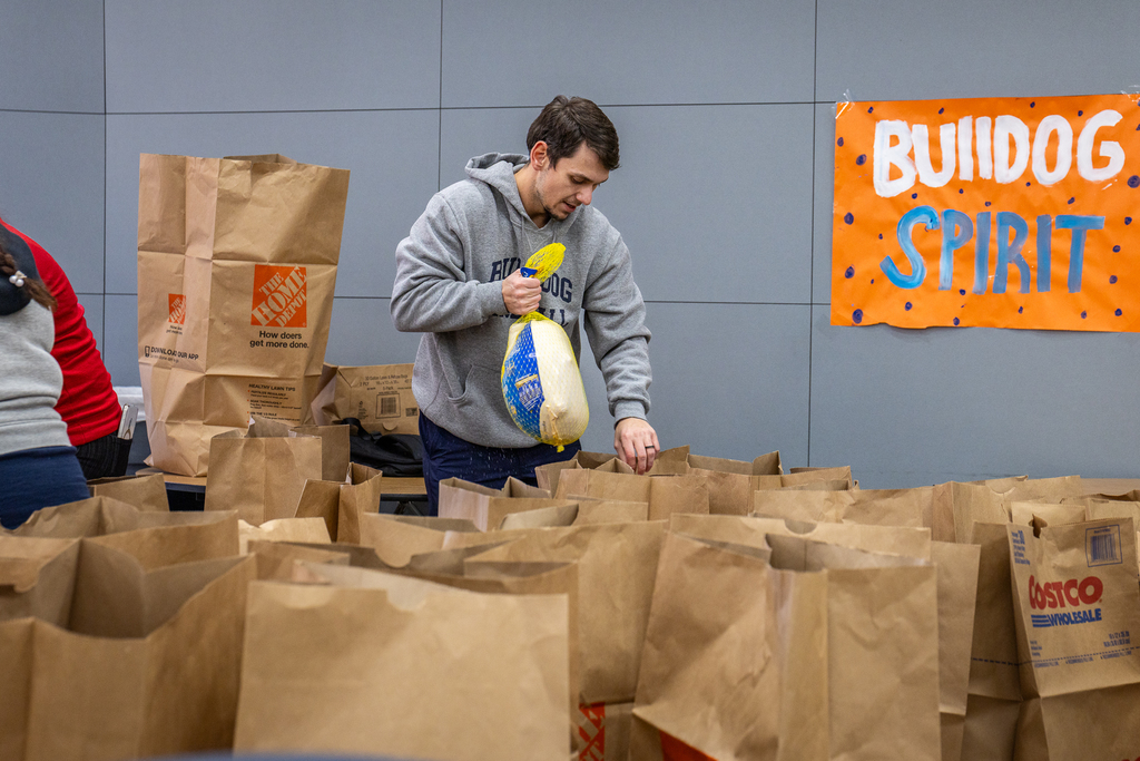North coach surrounded by large paper bags placing a frozen turkey in a bag