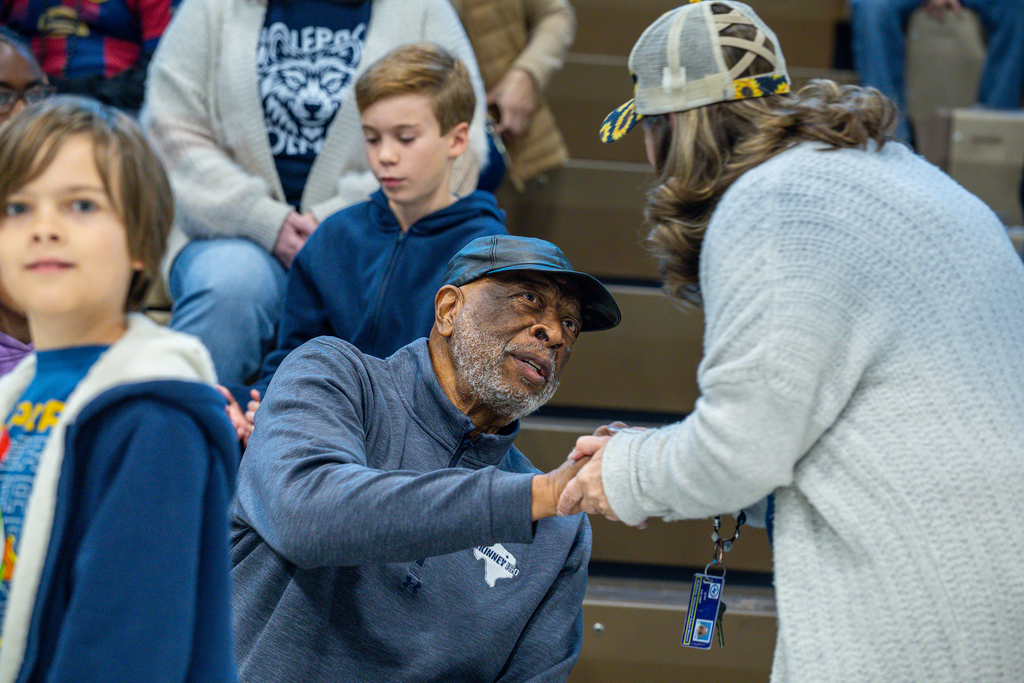 Larry Jagours shaking hands with a teacher as he sits in the gym at Slaughter